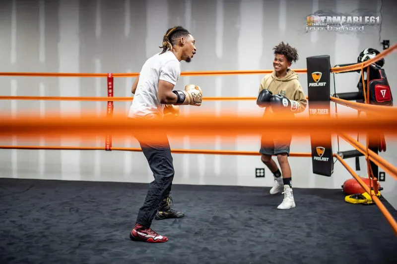 Coach and young boxer squaring up in the ring, orange ropes in the foreground