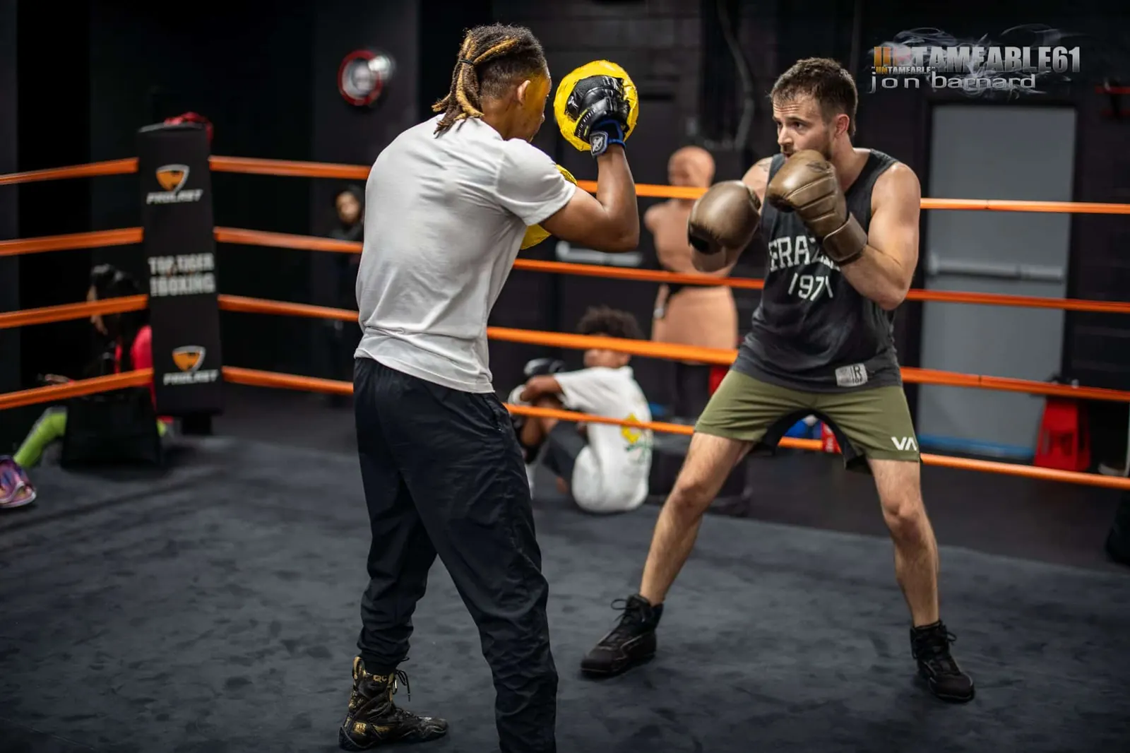 Coach holding focus mitts for a boxer in the ring corner