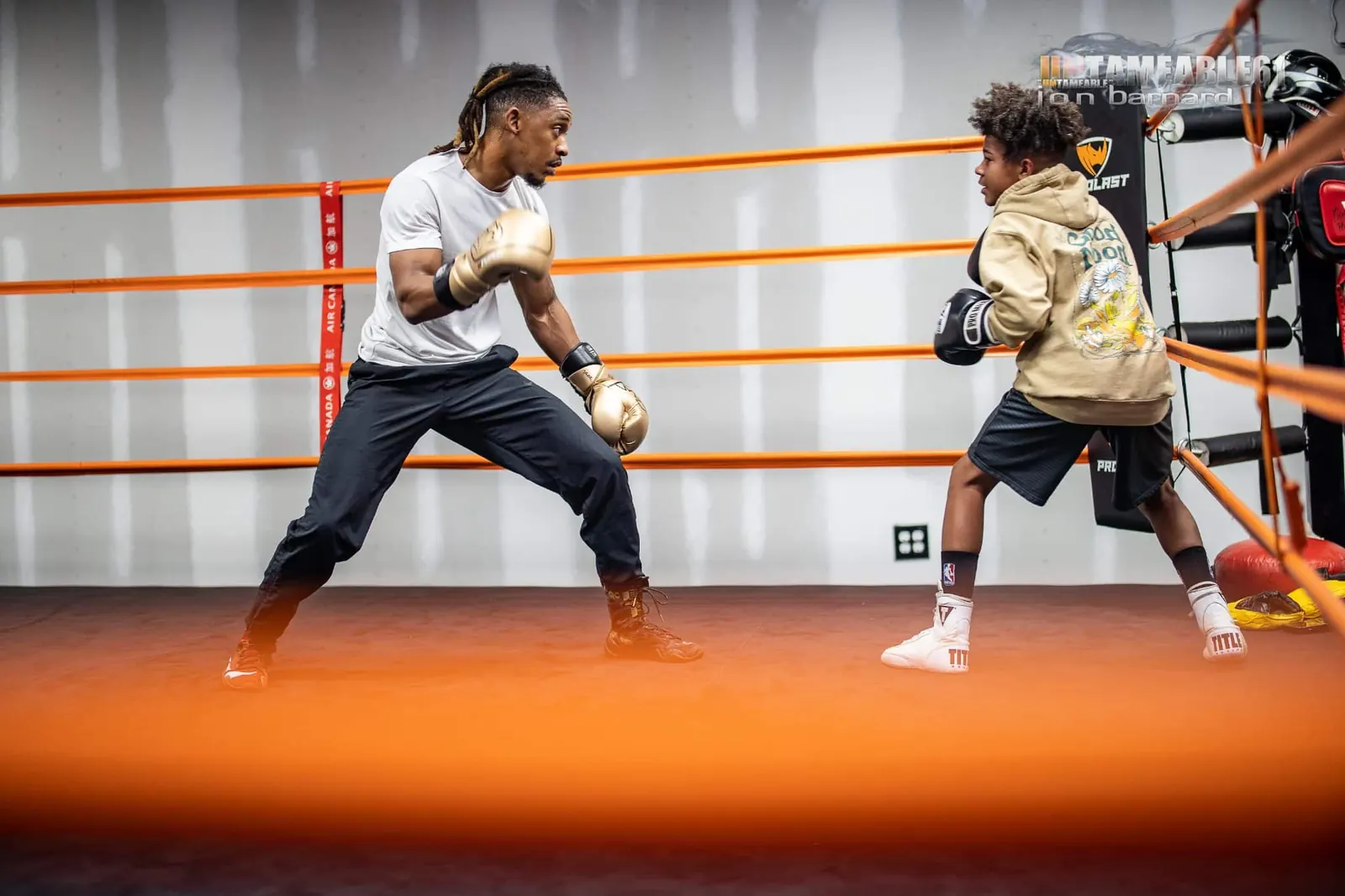 Coach sparring lightly with a young boxer on the orange ring canvas
